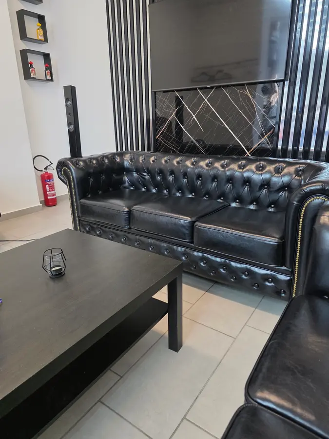 Schwarzes Chesterfield-Sofa vor einer Wand aus schwarzem Marmor und Lamellen